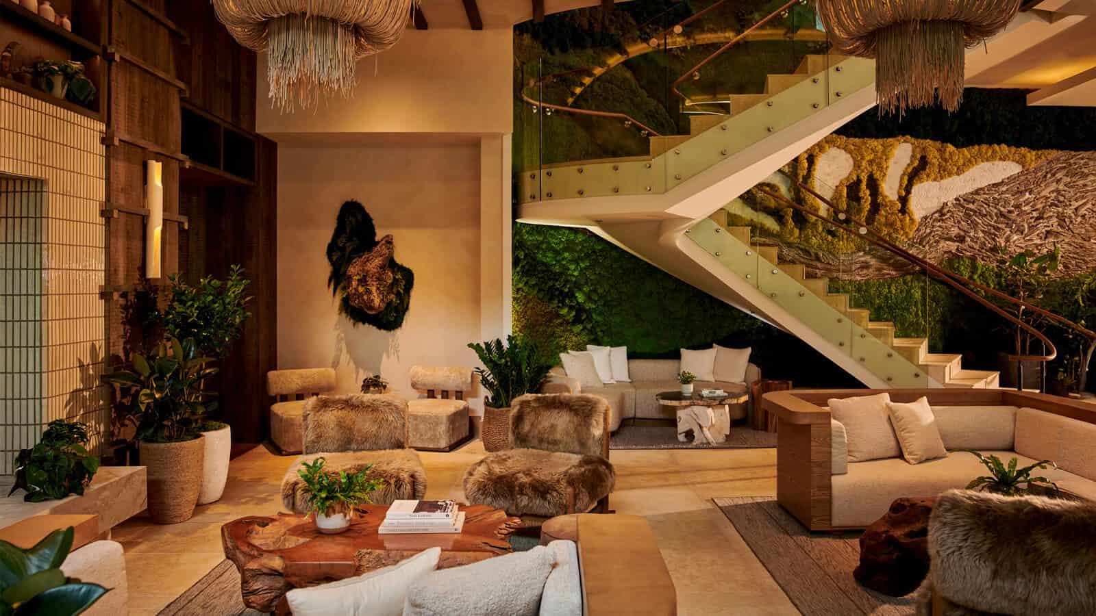 Modern hotel lobby at 1 Hotel South Lake Union with earthy decor, fur-covered chairs, green plants, and a glass staircase. This hidden gem features neutral tones and nature-inspired wall art for a cozy, inviting atmosphere.