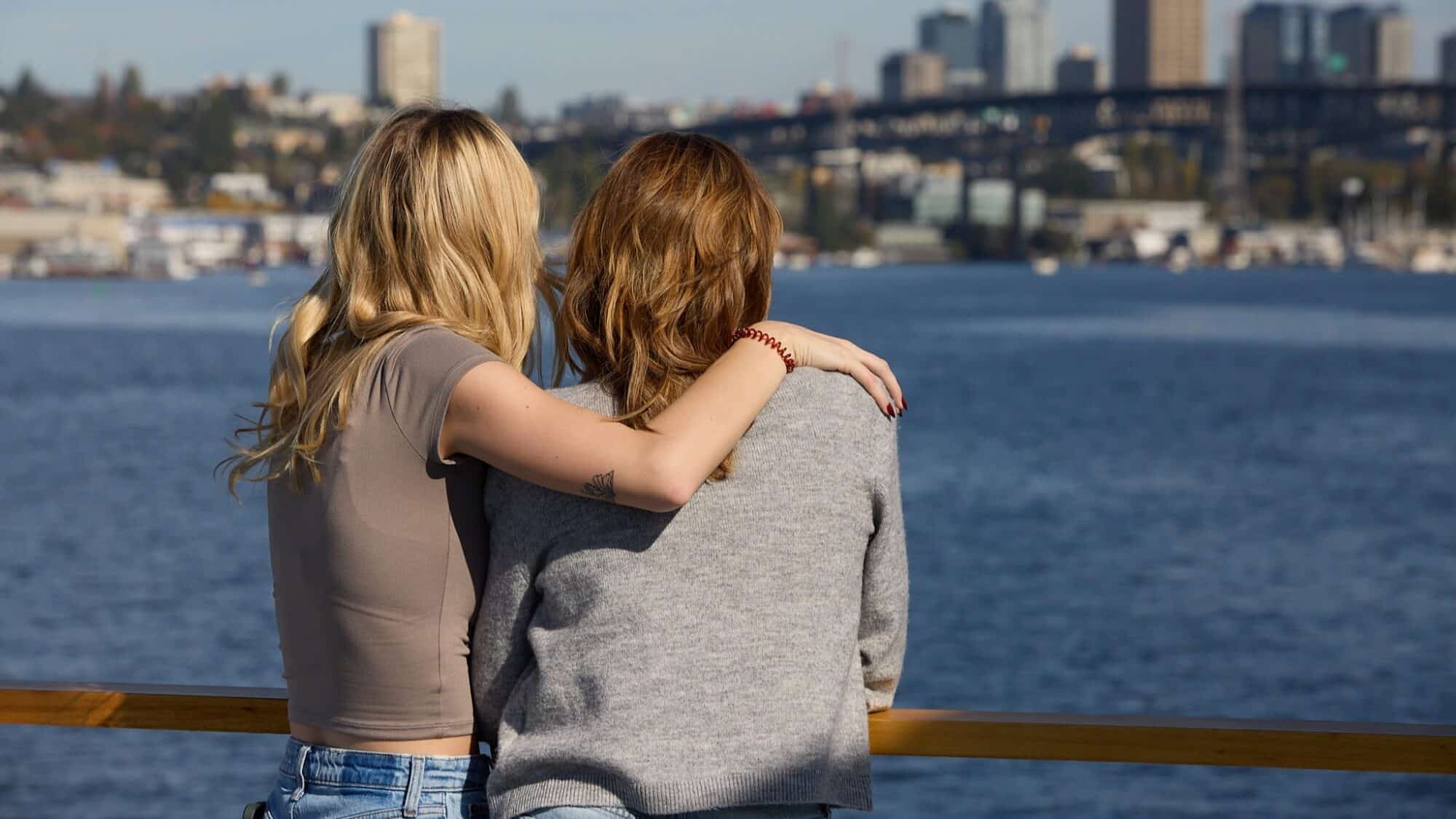 Two people stand side by side, one with an arm around the other, facing a body of water with a city skyline and bridge—capturing a perfect Seattle Mother’s Day moment.