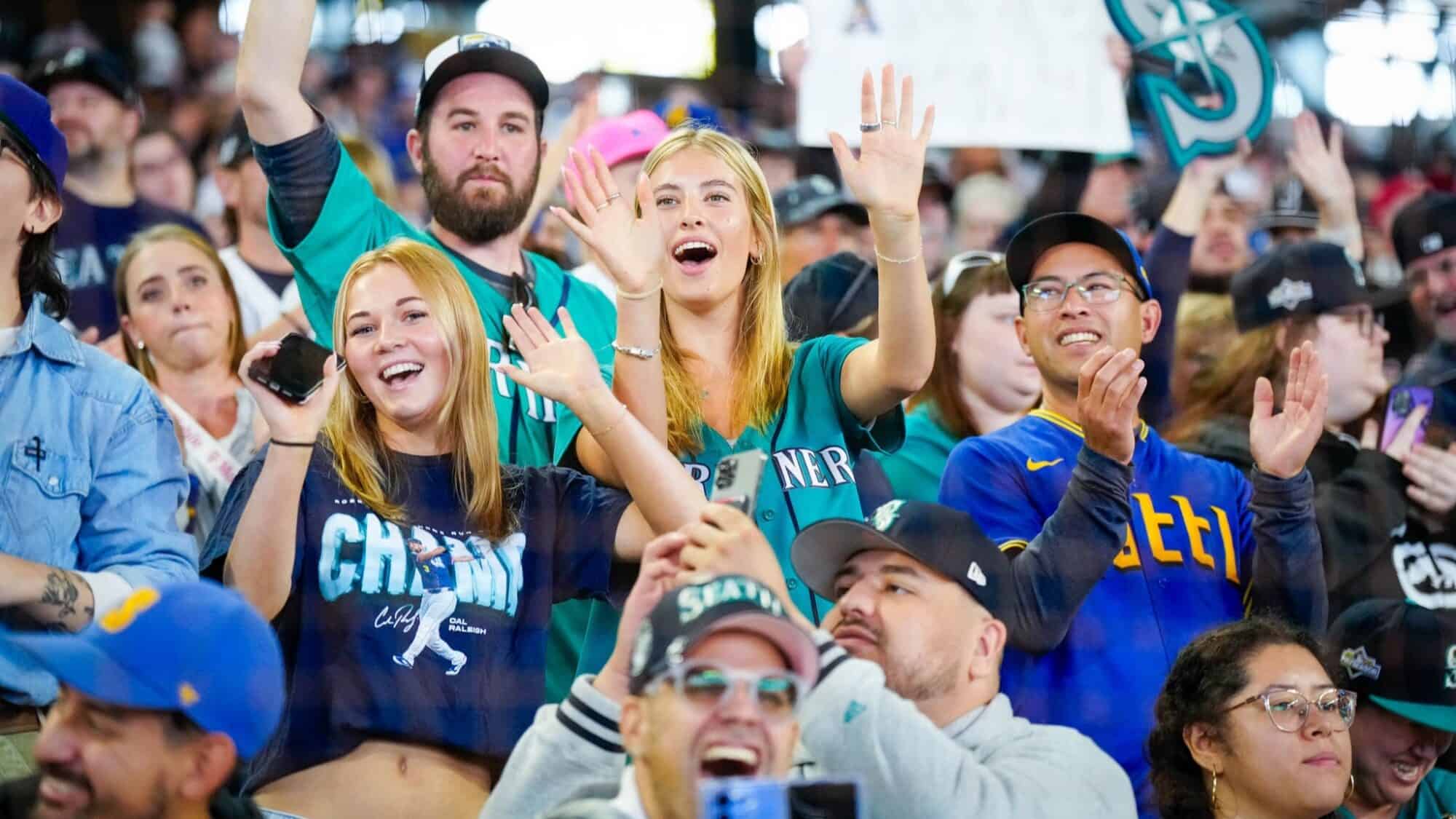 A crowd of enthusiastic fans wearing team jerseys and shirts cheer and wave at a sporting event.