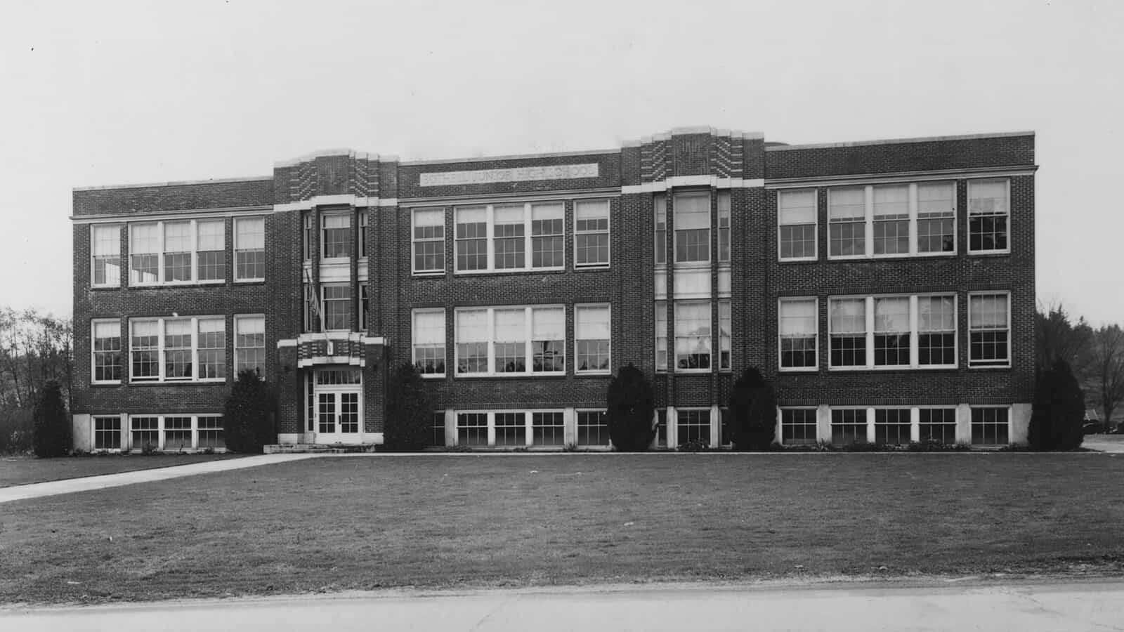 The Anderson School is a large, three-story brick building with many windows and a sign above the entrance, surrounded by lawn and shrubs, where lessons and preservation of history go hand in hand.
