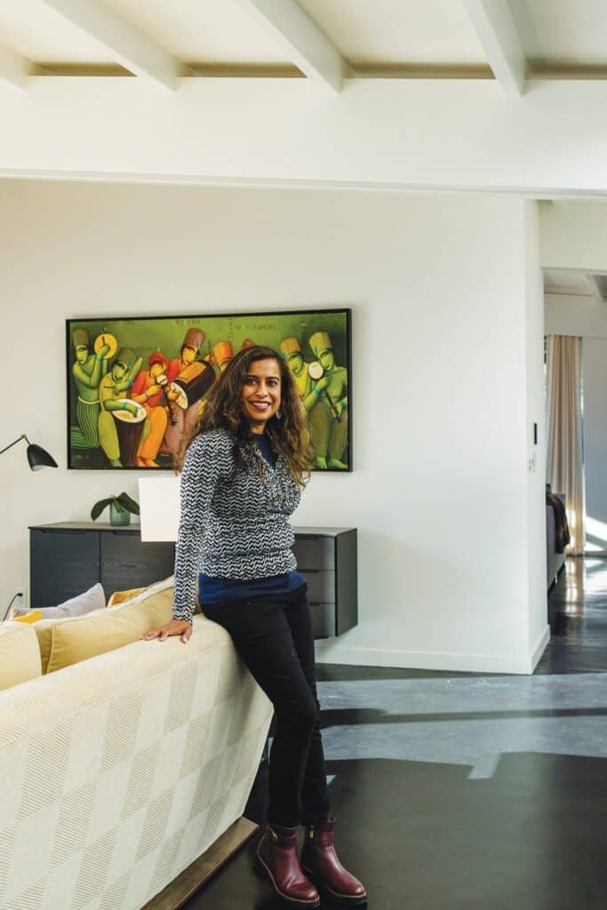 A person stands leaning against a sofa in a modern living room, which evokes the serenity of second homes, with abstract art on the wall and natural light streaming in from a window.