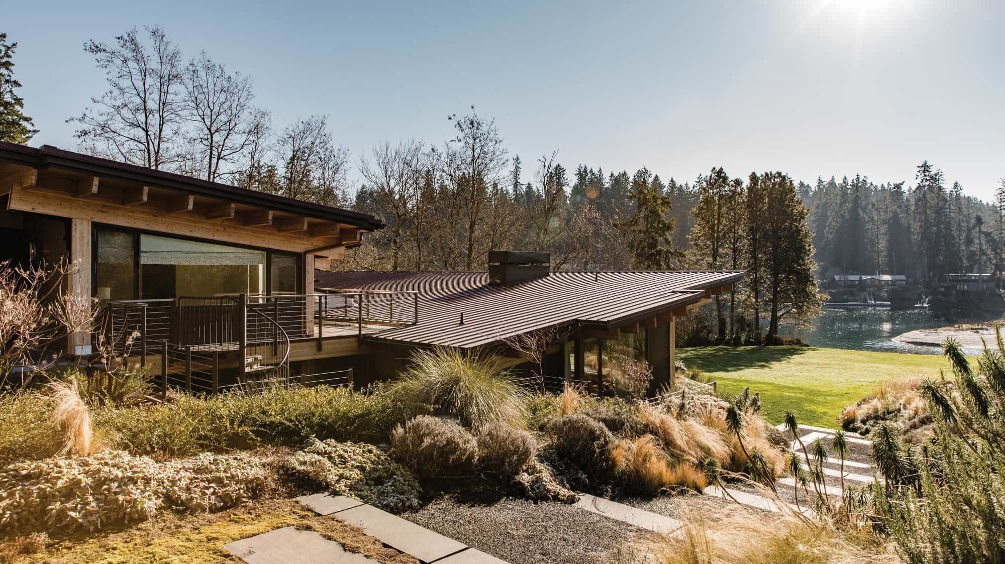 This modern house with large windows and a flat roof is a perfect second home, nestled among trees and greenery. It offers serene views of a body of water under clear skies, making it an ideal spot for those who dream of retiring on the beach.