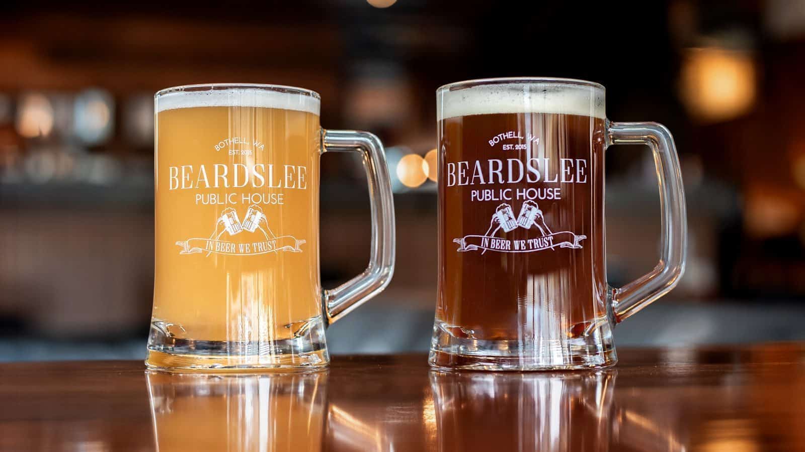 Two beer mugs from Beardslee Public House, often hailed as the best brewery in town, rest on a wooden table—one filled with light beer and the other with dark beer.