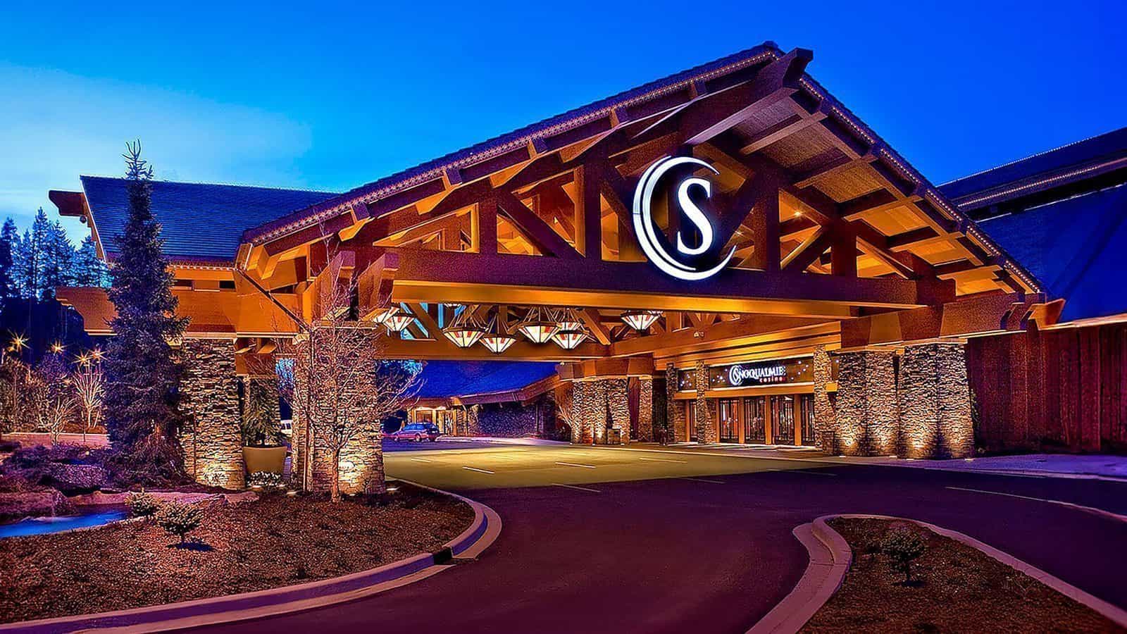 Exterior view of a building with a large entrance, featuring a wooden structure and a circular sign with the letter 'S'. The Snoqualmie Casino is beautifully illuminated at night, adding to its allure as possibly the best casino experience.