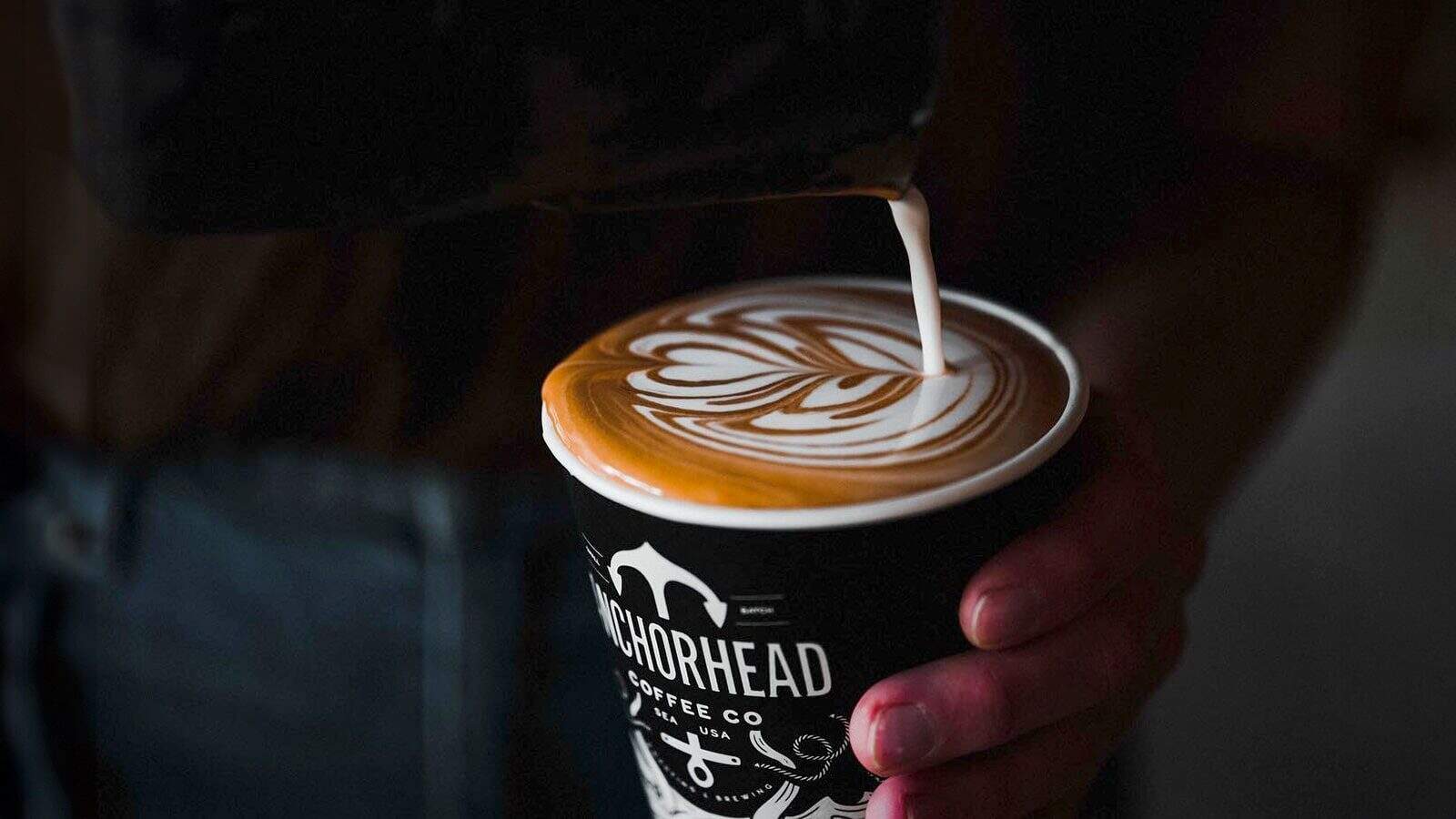 At one of the finest Seattle restaurants, a skilled barista expertly pours steamed milk, creating intricate latte art in a cup of coffee from Anchorhead Coffee Co.