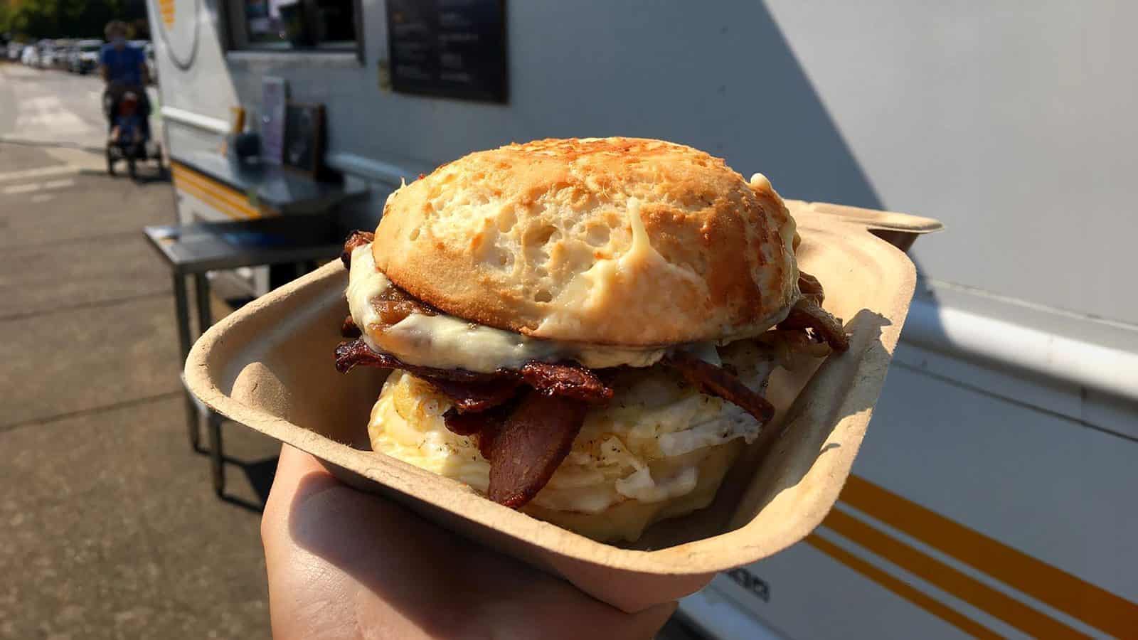 A hand holds a bacon, egg, and cheese sandwich in a biodegradable tray, perfectly capturing the essence of Seattle's breakfast-only food truck scene.