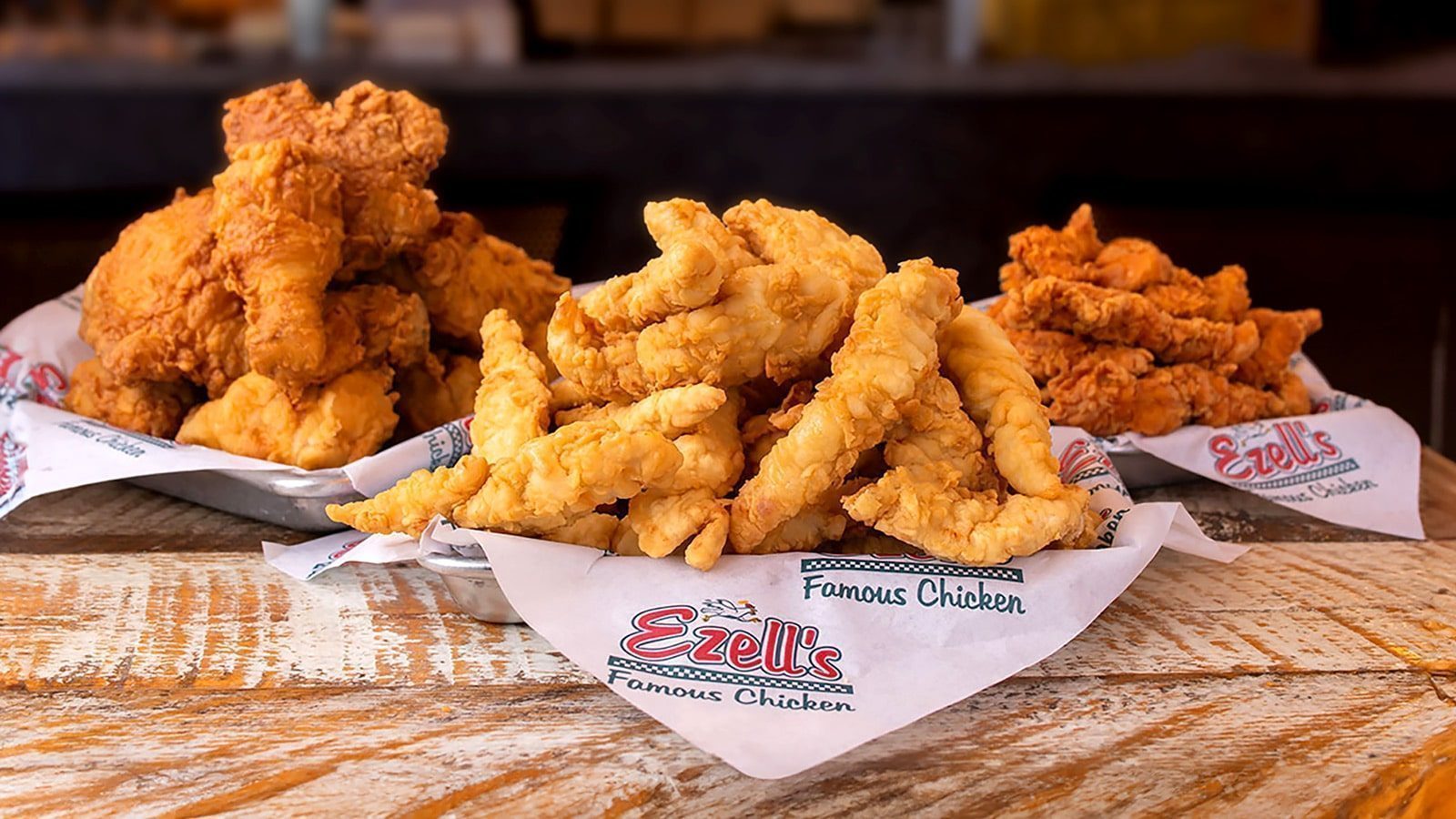 Plates of fried chicken and chicken strips rest on branded napkins at a new Seattle restaurant, all presented on a rustic wooden table.