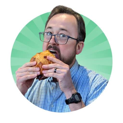 A person with glasses is eating a large sandwich while wearing a blue checkered shirt and a wristwatch, set against a green radial background.