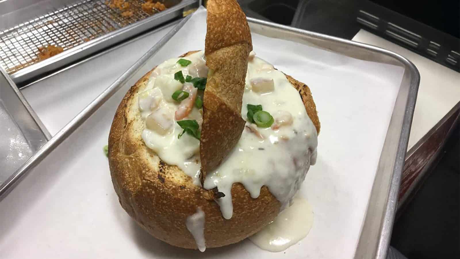 A bread bowl filled with creamy soup, topped with chopped green onions, sits on a tray lined with parchment paper at Counter Culture: Burien Fish House.