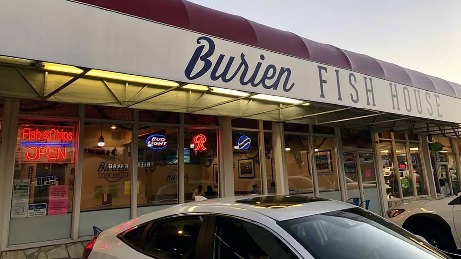 Exterior of Counter Culture: Burien Fish House with neon signs glowing in the windows, a red and white awning overhead, and a white car parked in front.
