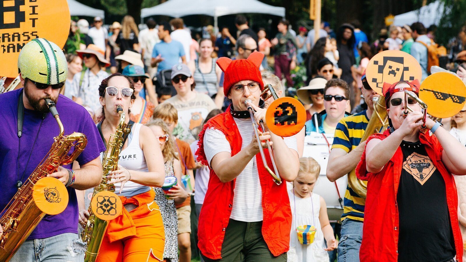 A costumed brass band with pixelated-themed instruments entertains crowds at an outdoor event, bringing playful energy to the Seattle Design Festival.