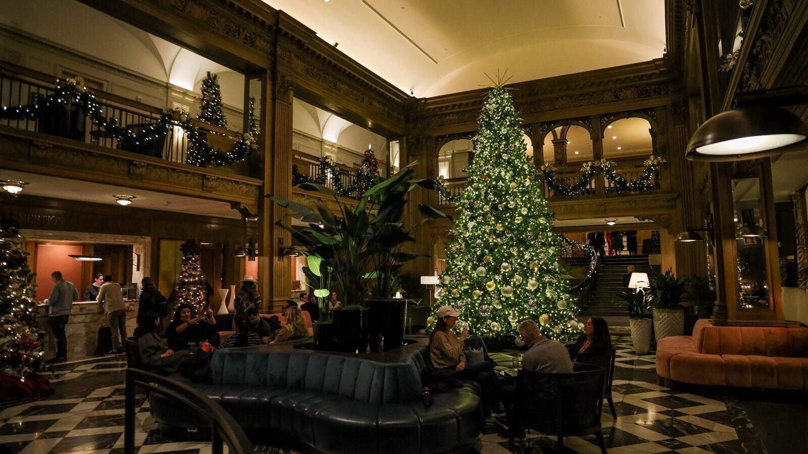 The hotel lobby, perfect for a Seattle New Year for all types, is beautifully decorated with a large Christmas tree and festive garlands. Guests relax on couches in the warmly lit area, soaking in the holiday ambiance.