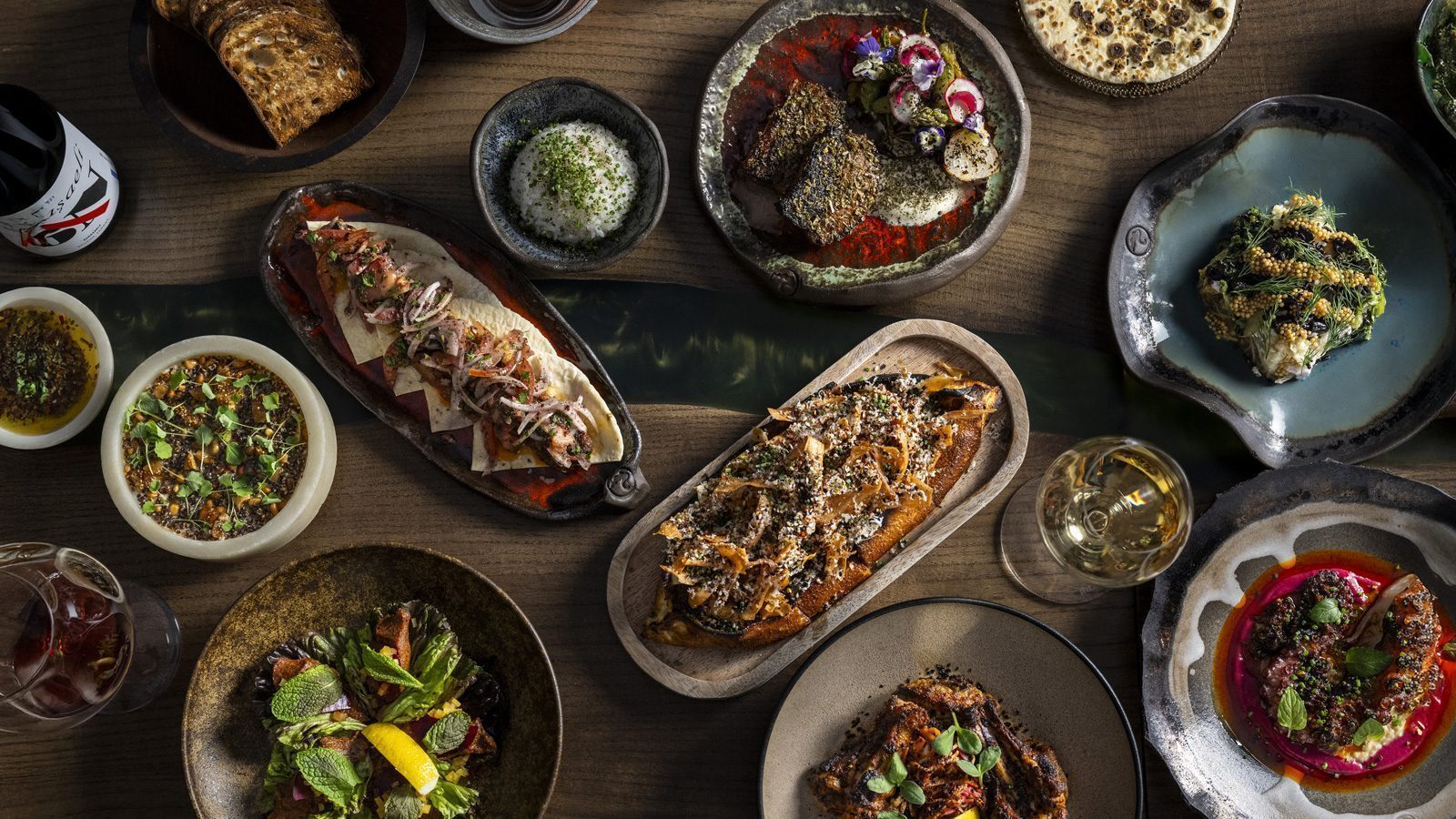 An aerial view captures an assortment of decorative dishes showcasing gourmet foods on a wooden table, set for a Seattle New Year celebration, complete with glasses of white and red wine suitable for all types.