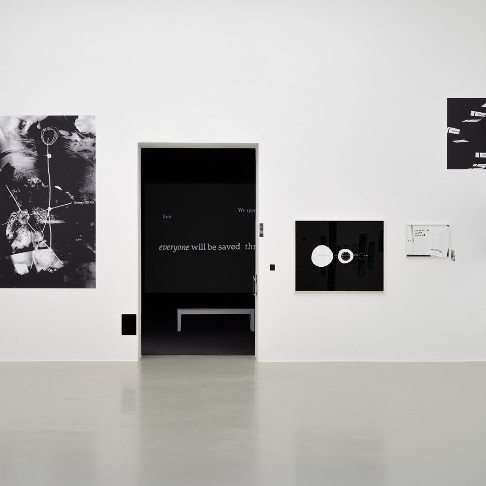 A minimalist art gallery wall featuring black and white abstract artwork, with a doorway revealing a bench and projected text in the dark room beyond—a must list experience for 08-21-2025.