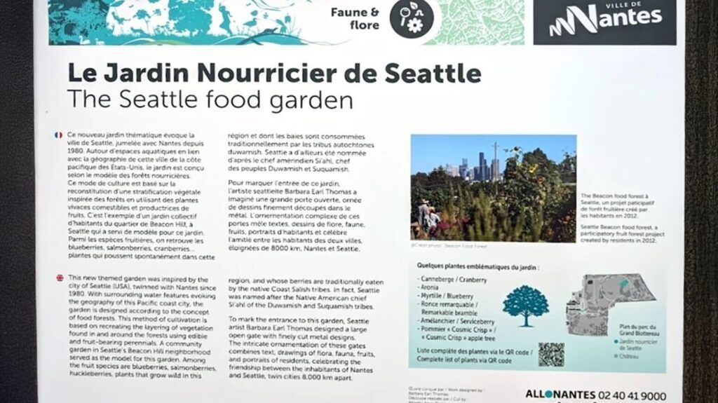 Informational display board about "Le Jardin Nourricier de Seattle" (The Seattle Garden), featuring text, a list of plants grown, and a cityscape photo that links the garden to both Seattle and inspiration from France.