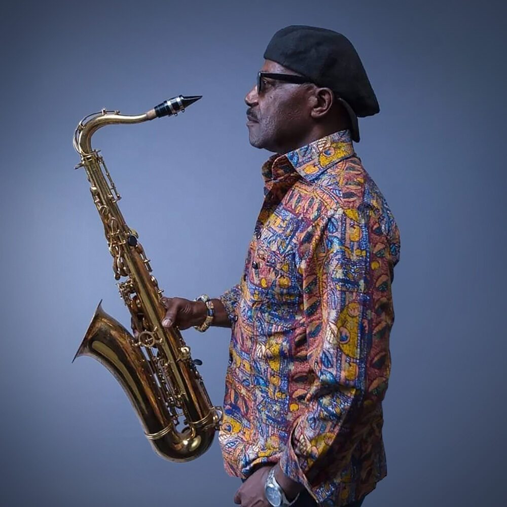 A man in a patterned shirt and beret stands in profile holding a saxophone against a plain background—a true Must List moment for 07-10-2025.