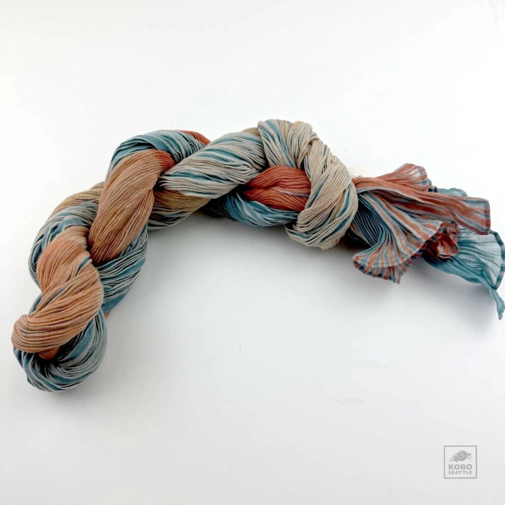 A twisted skein of multicolored yarn in muted shades of blue, beige, and rust, placed on a white background.