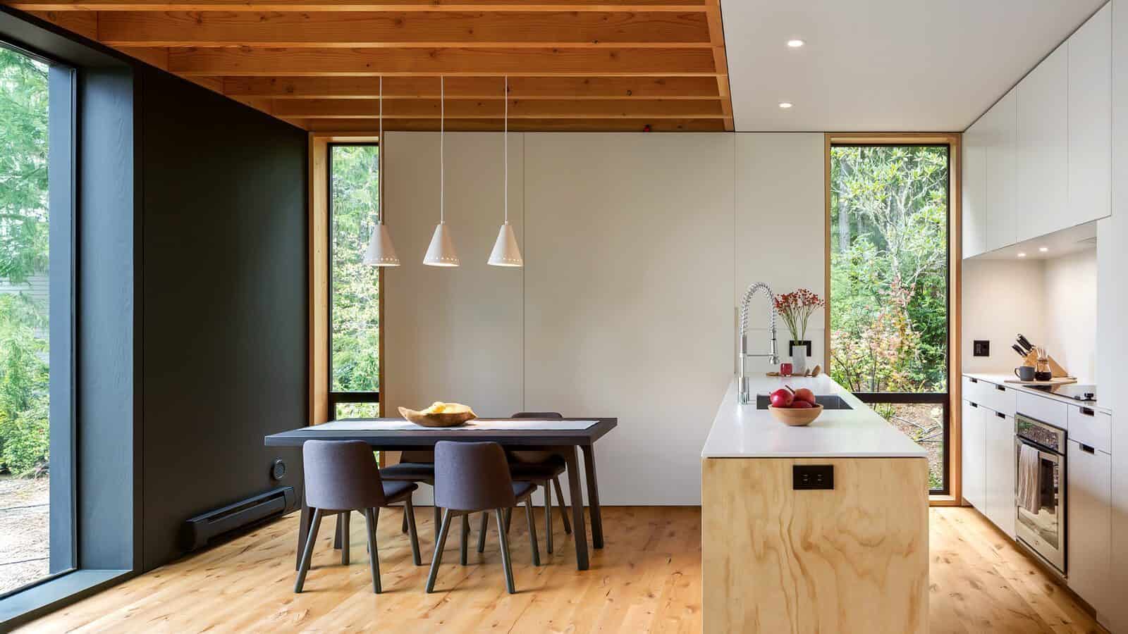 Modern kitchen and dining area with wooden floors, minimalist furniture, large windows, and pendant lights above the dining table—perfect for second homes or summers in the waterfront.