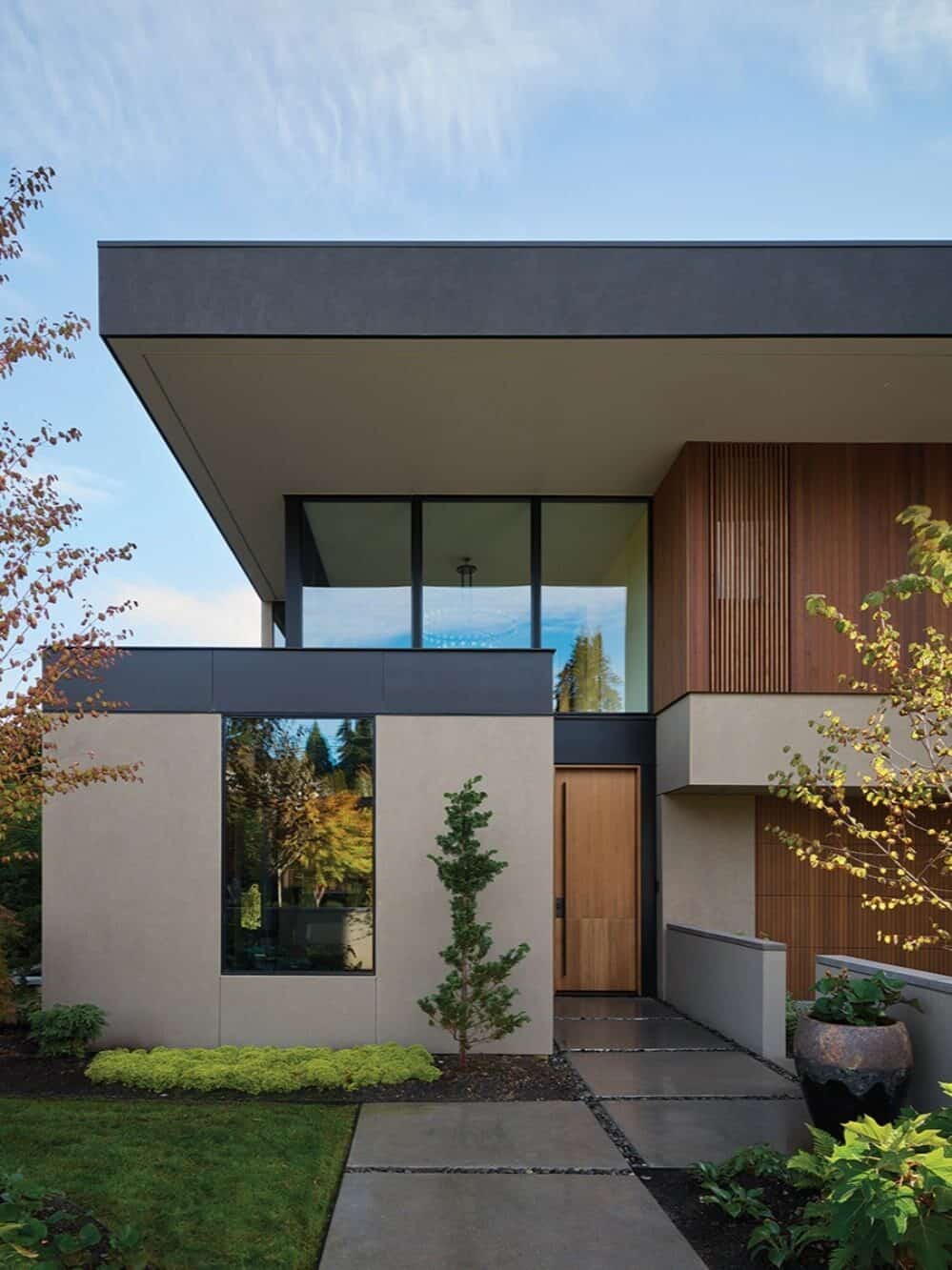 A modern two-story custom-built home with large windows, flat roof, wood and concrete exterior, landscaped front yard, and a wooden front door—perfect for boosting your home remodel value.