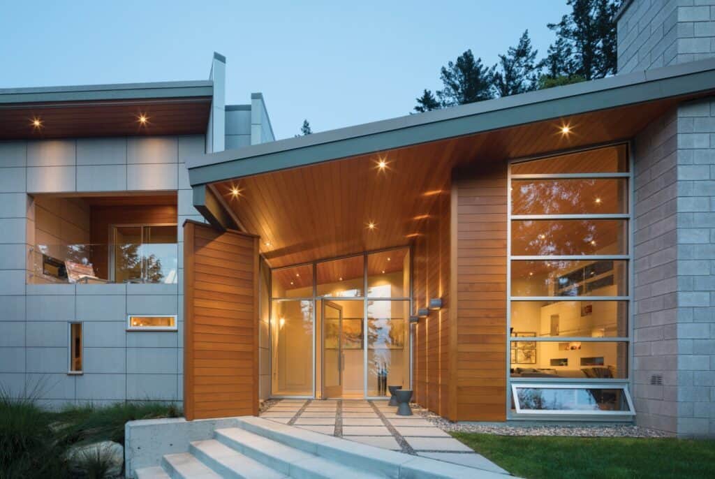 Seattle home design aesthetic shines through this modern house exterior with large glass panels, wooden accents, and an angular roof. Steps lead to a glass entrance under a wooden overhang, embodying the city's unique style.