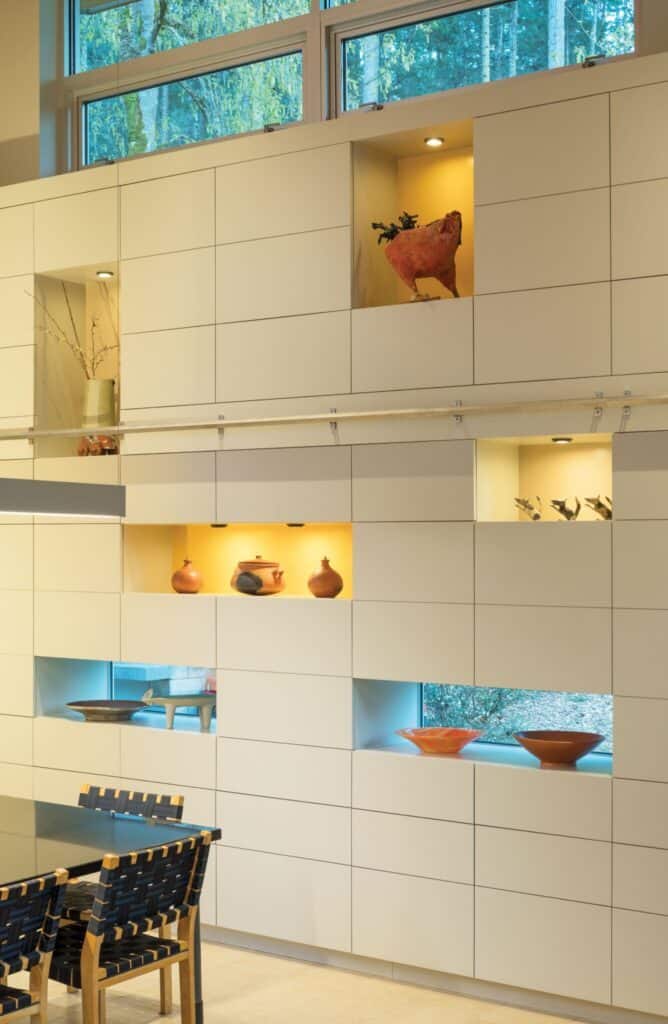 Modern kitchen wall with built-in shelves displaying decorative pottery and plants, illuminated by small lights. The interior design showcases the distinctive Seattle home design aesthetic, with large windows providing ample natural light.