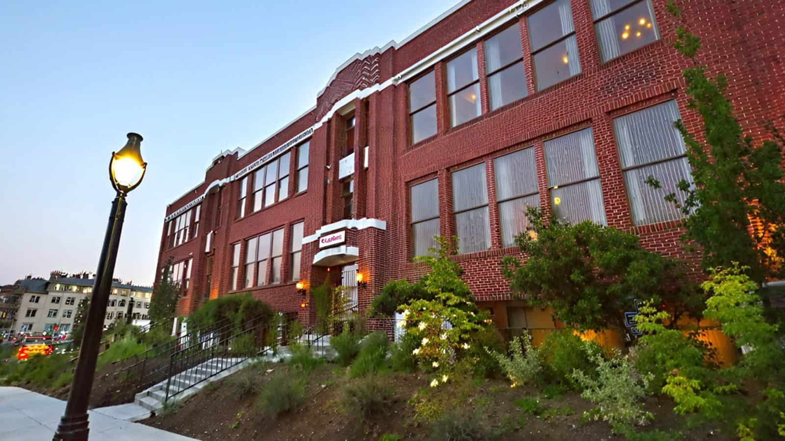 A large red brick building with multiple windows and a white sign near the entrance stands tucked away in Bothell. Surrounded by greenery, it is situated along a pathway with a street lamp, making it one of Hidden Washington’s charming finds.
