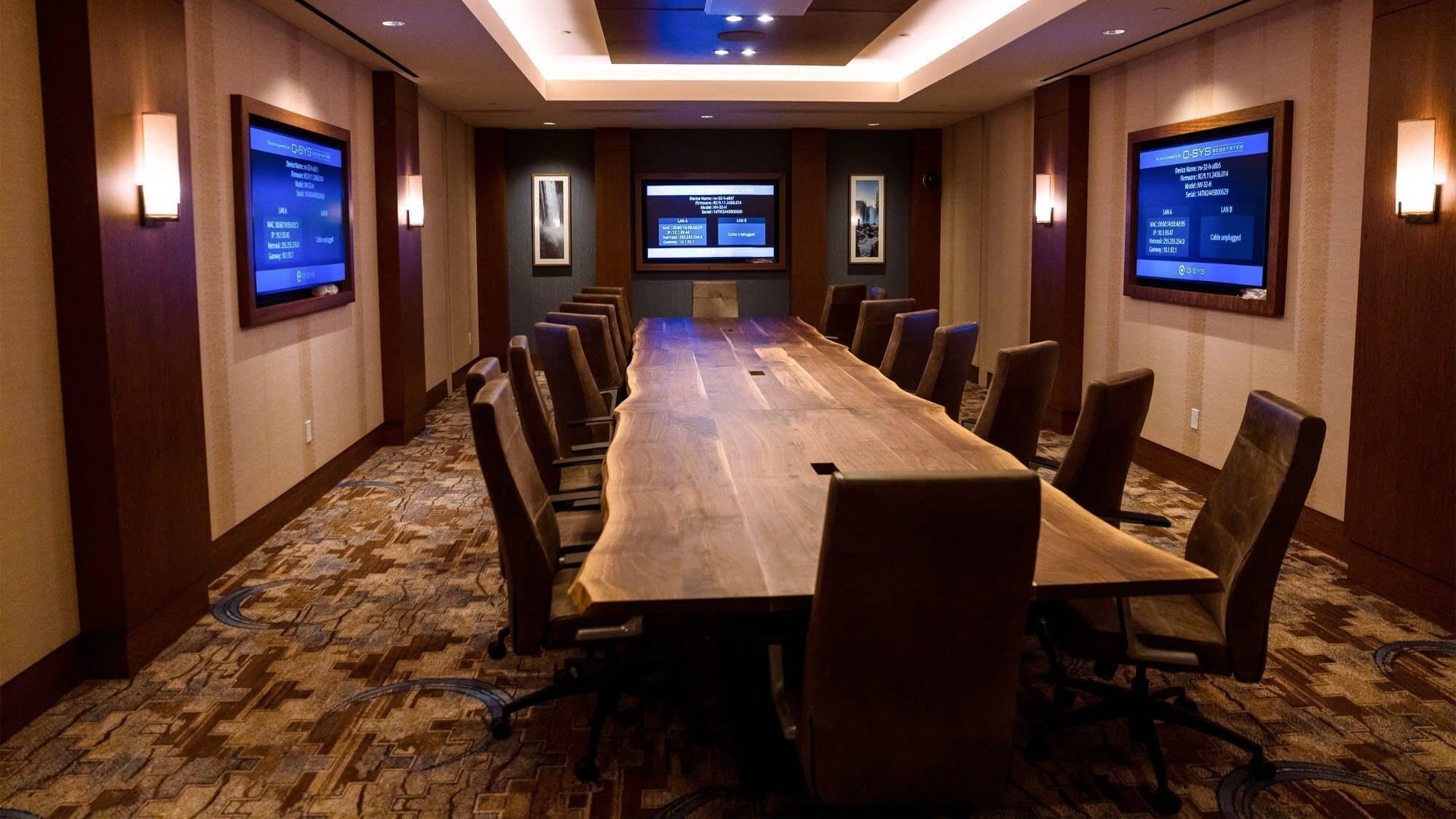 A modern conference room with a long wooden table, leather chairs, three wall-mounted screens, and dim lighting—perfect for gaming strategy sessions at Snoqualmie Casino & Hotel.