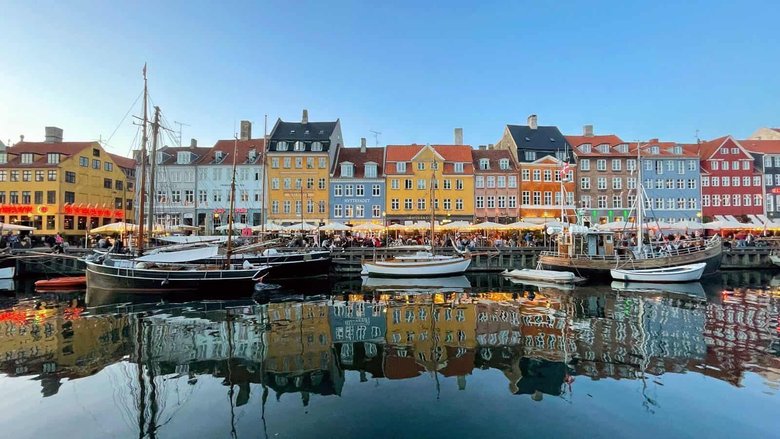 Colorful buildings and boats line a canal under a clear blue sky, their reflections dancing on the water. This enchanting scene could easily be one of Ten Top Travel Destinations from Seattle for 2025, capturing the hearts of travelers with its vibrant charm.