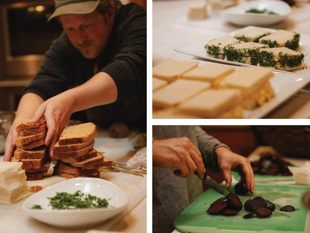A person stacks sliced bread, another cuts dark vegetables on a green board—echoing Lessons from the Land—and plates of tea sandwiches with herbs are displayed on a counter.