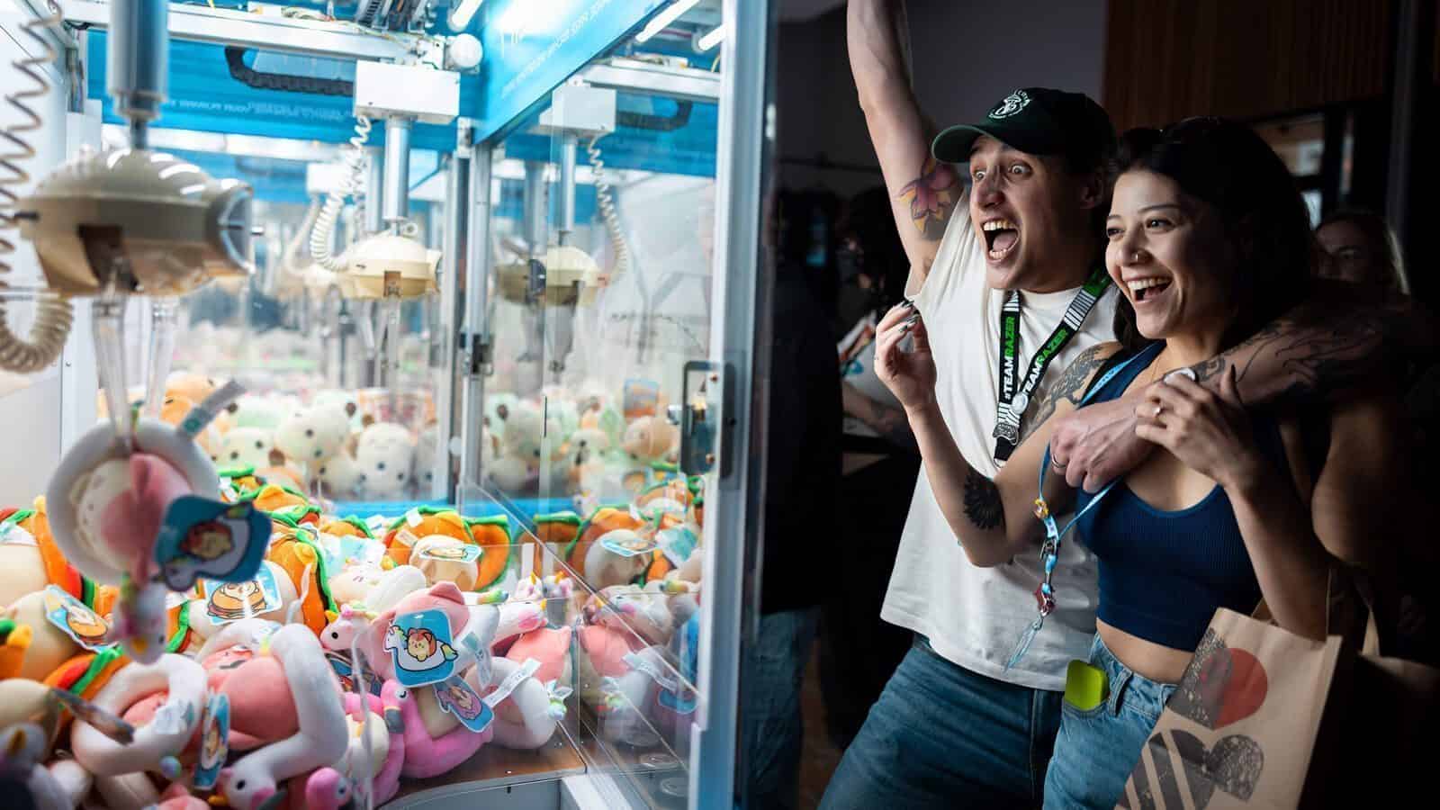 Two people excitedly play a claw machine filled with plush toys, smiling and celebrating as they watch the game in action.