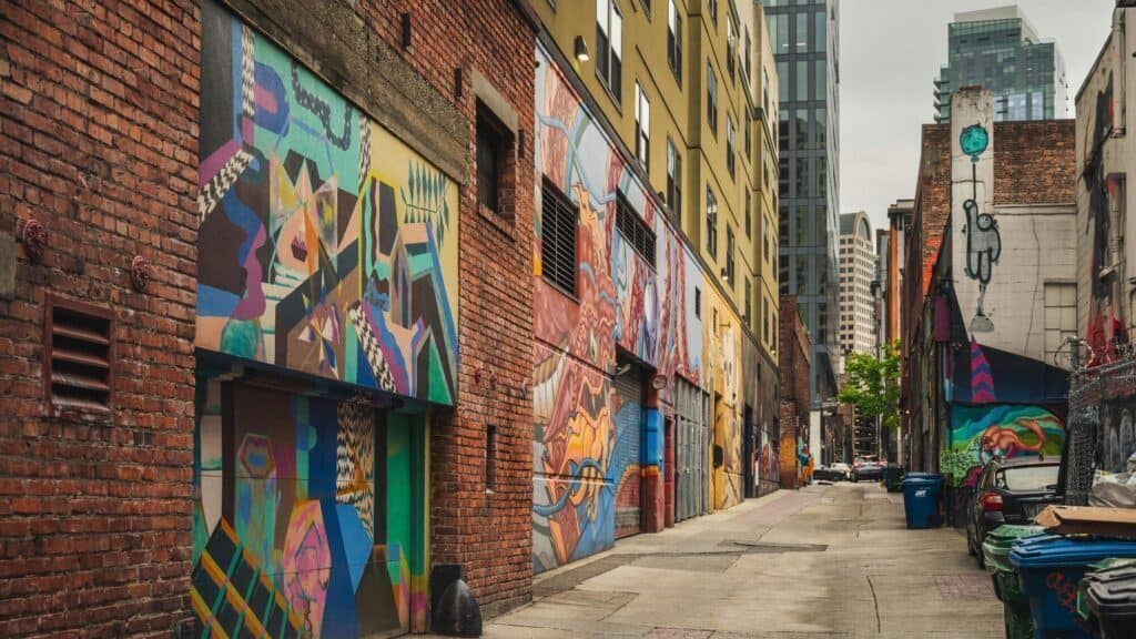 A city alleyway in Seattle lined with colorful abstract murals on building walls reminds passersby that Art Matters, with trash bins along the side and tall modern buildings rising under a cloudy sky.
