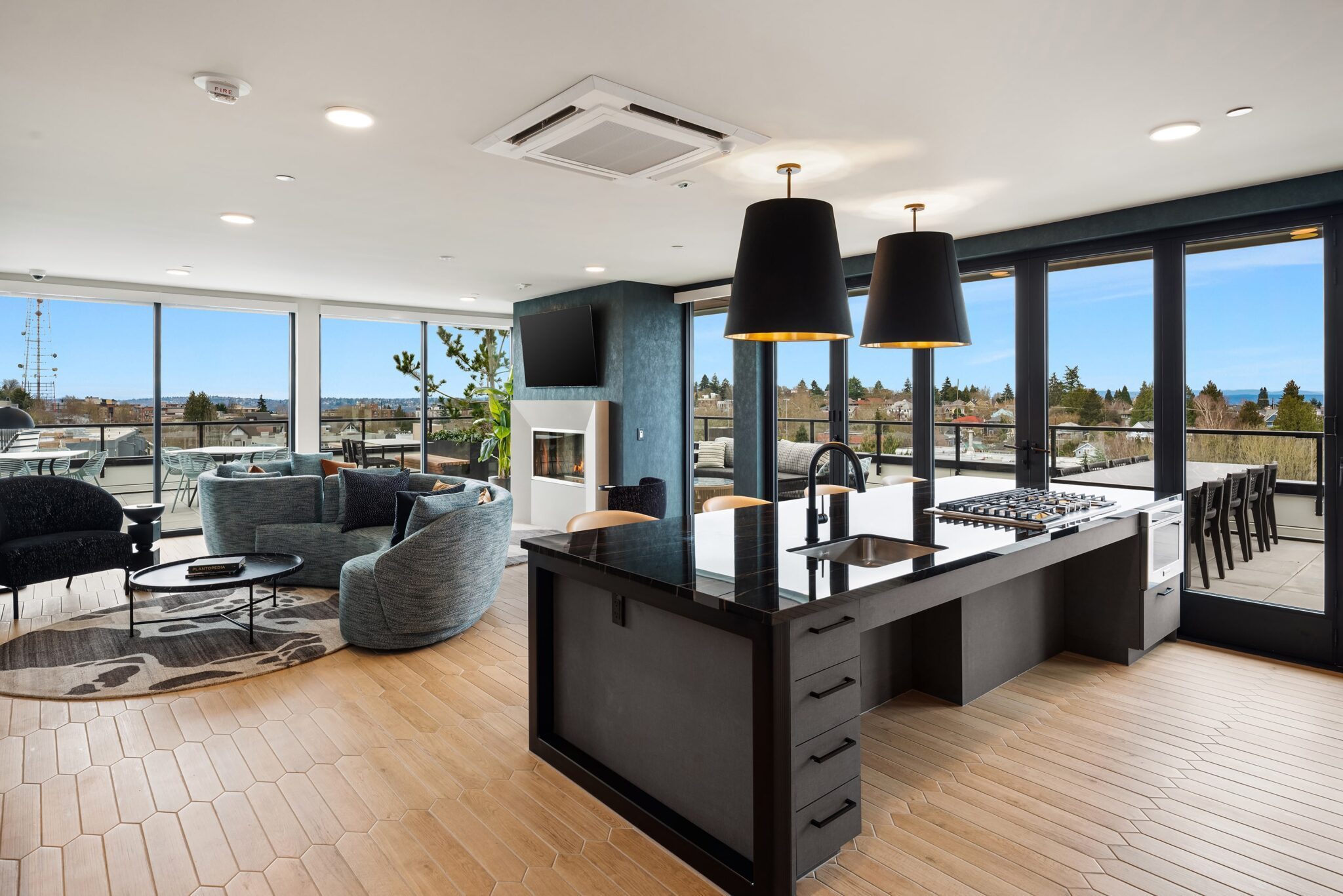 The modern open-plan living room and kitchen blends a Queen Anne style with a sleek black island, hanging lights, and large windows offering city views. Enjoy comfortable seating by the fireplace or step onto the outdoor balcony area for fresh air.