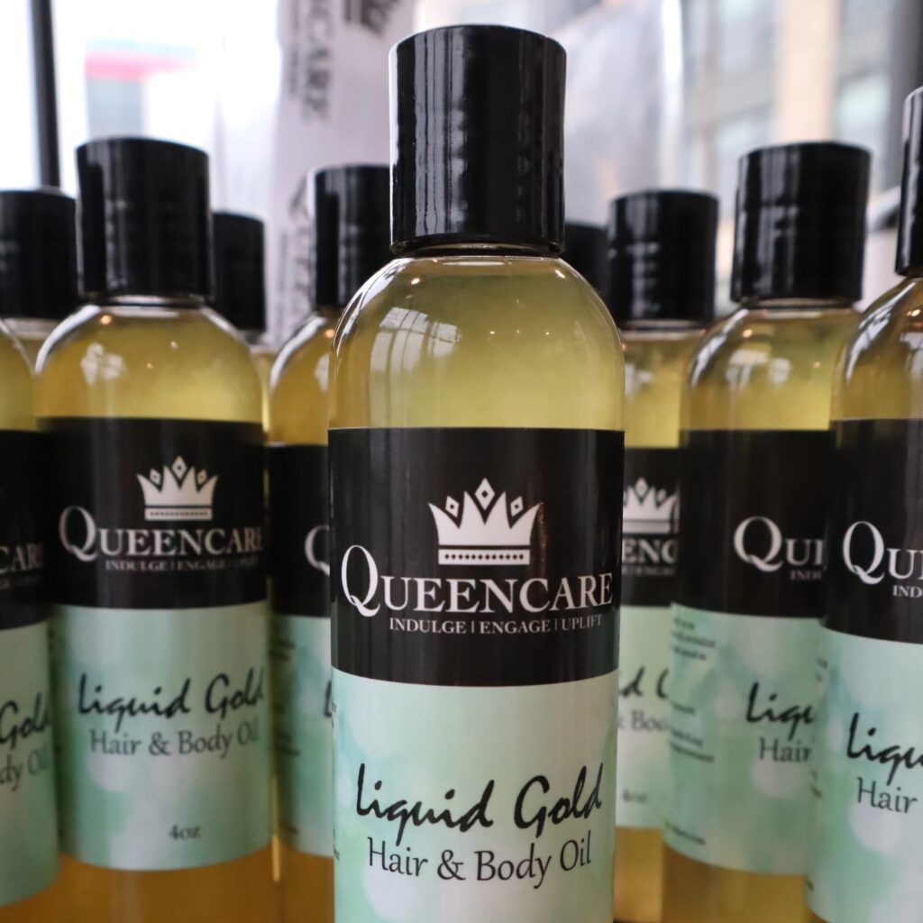 Several bottles of Queencare Liquid Gold Hair & Body Oil are arranged closely together on a surface, with product labels visible.