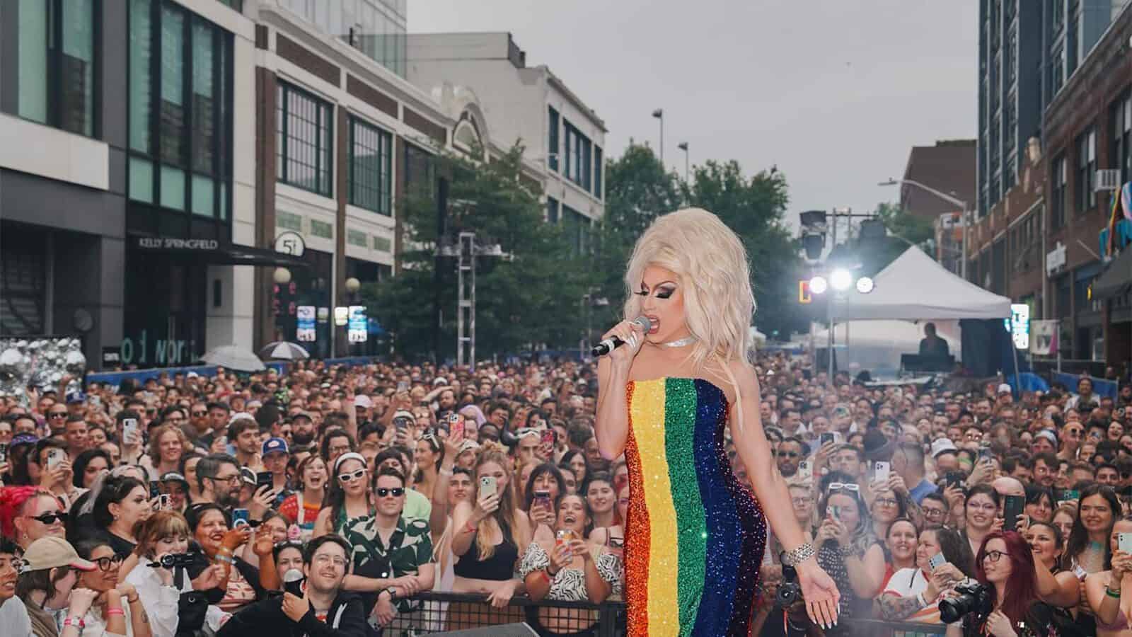 A drag performer in a rainbow dress sings onstage to a large crowd at an outdoor event in an urban area, as vibrant celebrations honor Seattle’s rich LGBTQIA+ history.