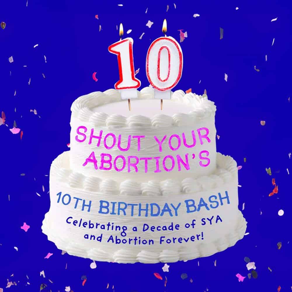 A white two-tier cake with "Shout Your Abortion’s 10th Birthday Bash" written on it and candles shaped like the number 10, set against a blue background with confetti—add this Must List event on 09-04-2025 to your calendar!.