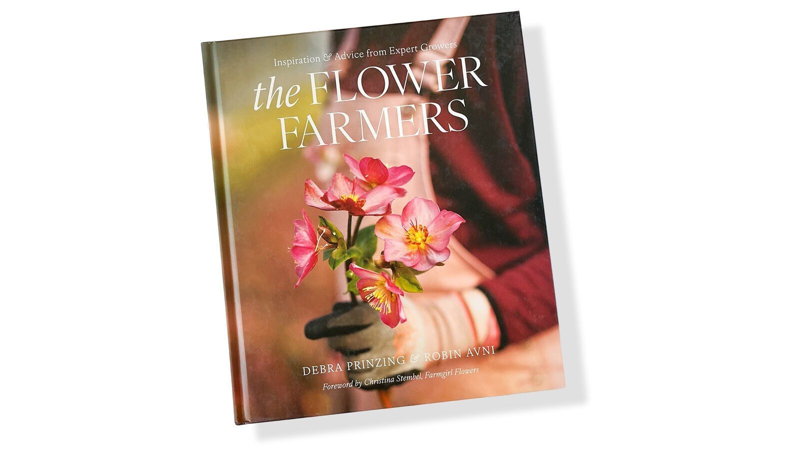 The cover of "The Flower Farmers" book, featuring a close-up of hands holding pink, seasonal and sustainably harvested flowers. Author names Debra Prinzing and Robin Avni are shown. New book promotes the use of locally grown blooms.