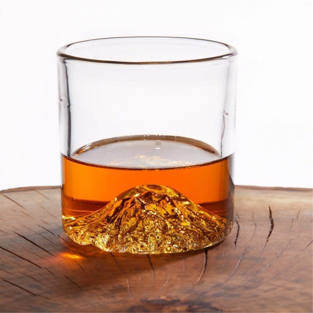 A glass of amber-colored liquid sits on a wooden surface; the glass features a mountain-shaped base inside—an inspired find for Seattle Mother’s Day gifts from any thoughtful Seattle gift guide.