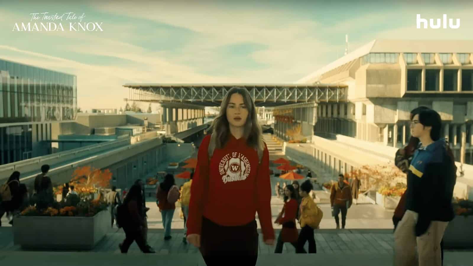 A young woman in a red "University of Washington" sweatshirt walks through a modern university campus, reclaims her story much like Amanda Knox did; students and outdoor seating are visible in the background.