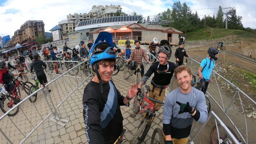 A group of mountain bikers, some wearing helmets and gear, wait in line with their bikes near a lift station in Leavenworth. Buildings and trees are visible in the background, showcasing the charm of Hidden Washington. This destination offers all-year outdoor adventures.